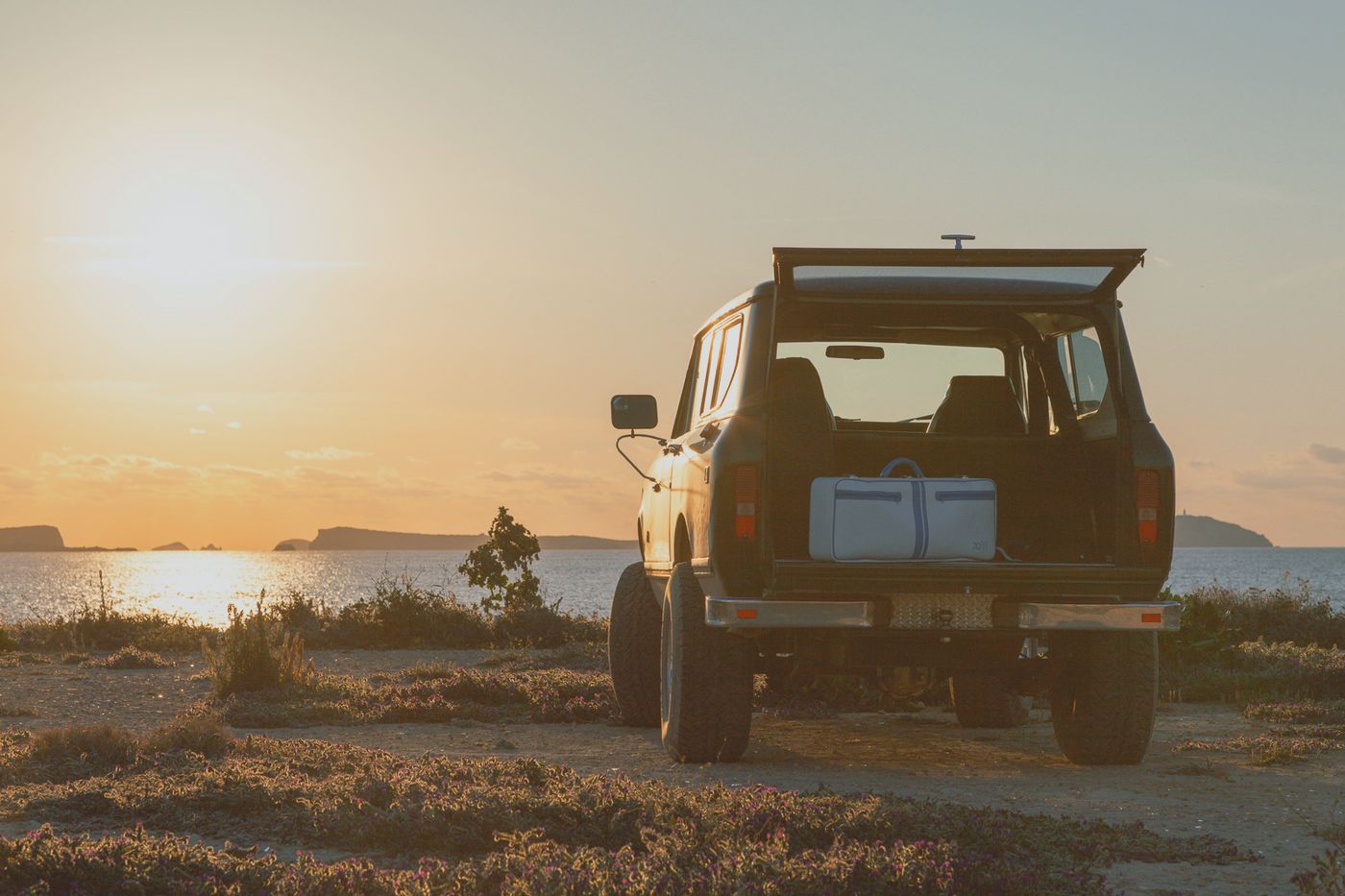 Geländewagen am Meer im Abendlicht, im geöffneten Heck der Tenniskoffer Jim