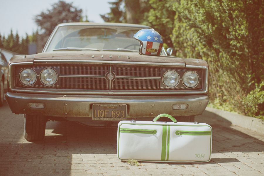 Grüner Tenniskoffer Jim vor einem Dodge Coronet mit Sternenhelm auf der Haube